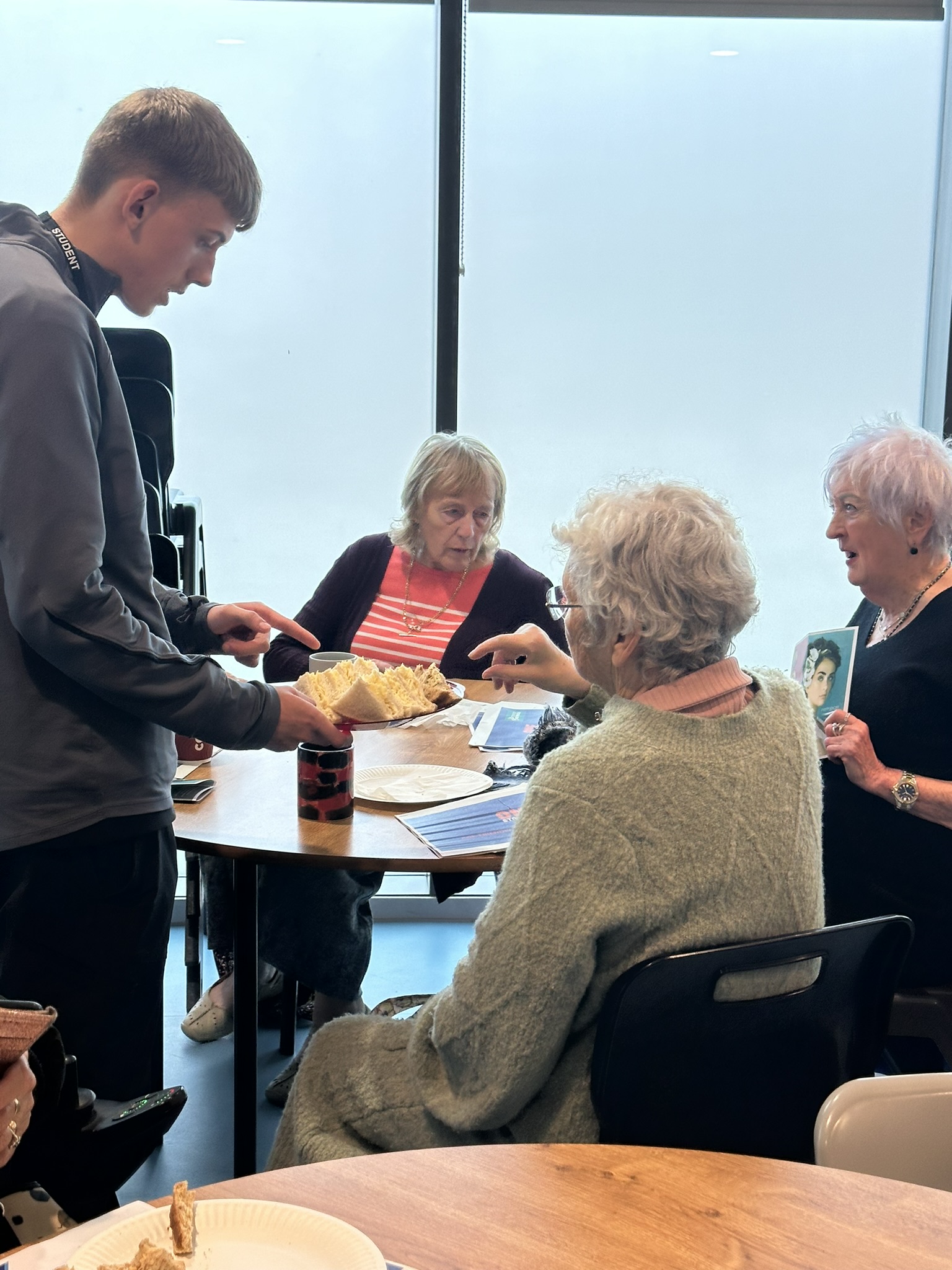 Elderly ladies sat at a table talking to a student