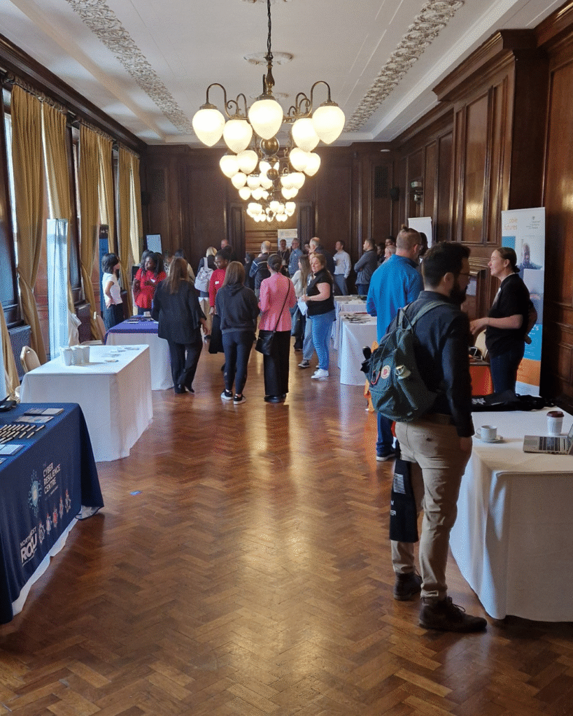 Large wood-paneled room set up for an event, with tables displaying materials and people walking around or talking near the displays.