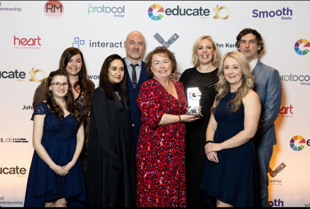 Group of nine people standing in front of a sponsor-branded backdrop at the Educate North Awards, with one person holding a community engagement award.
