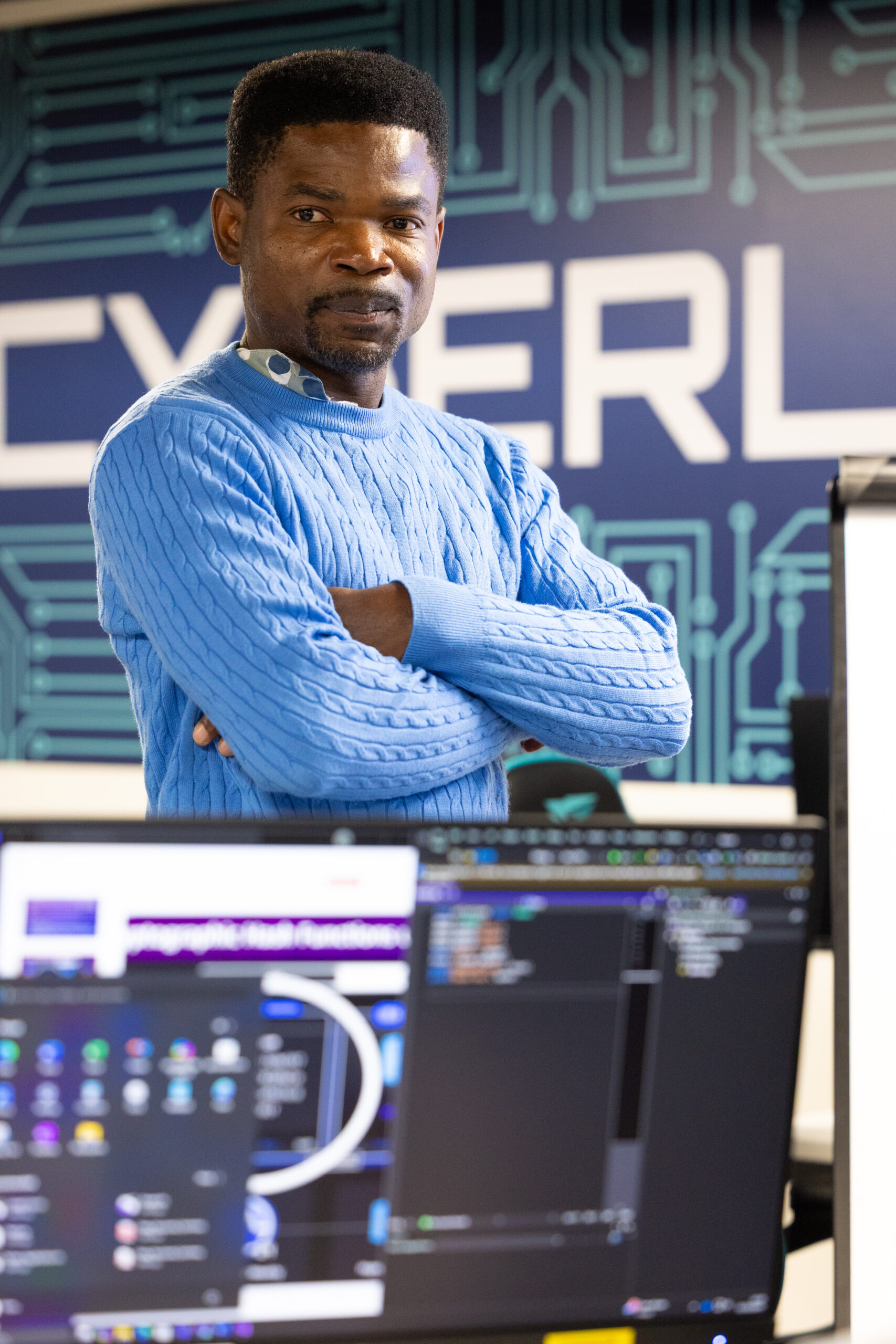 Brand New Cyberlab classroom with coding software displayed on monitors and a student standing in front of a digital-themed wall.